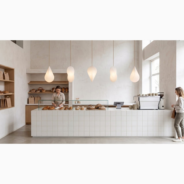 Five Oh Lloyd! pendant lights line up over a counter in a bakery. Each light is installed at a different orientation, thus displaying different profiles of the Oh Lloyd's unique form.