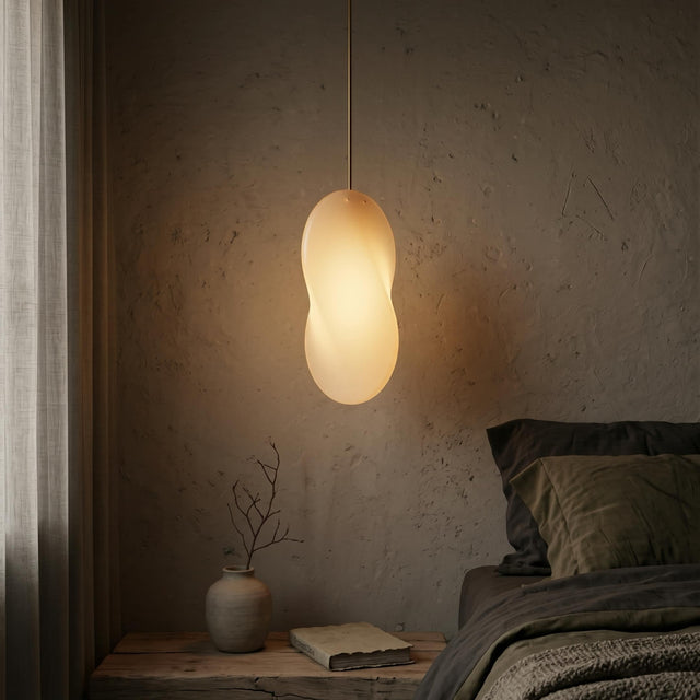 An Oh Lloyd! pendant light hangs over a bedside table in a dimly lit bedroom. Oh Lloyd's figure-of-8 profile is visible as it casts a soft shadow on the textured plaster wall behind it.