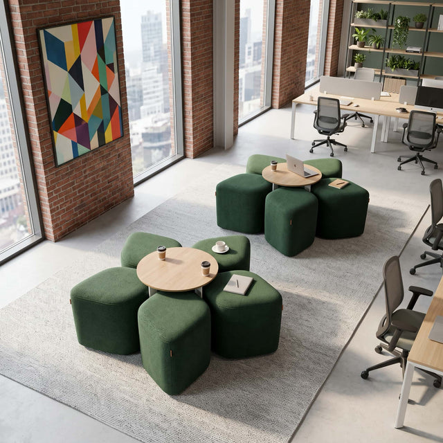 A modern breakout area in a workplace features two green Blossom seating systems with Oak tables. Each Blossom consists of 5 upholstered poufs arranged around a central table, collectively forming the shape of a 5-petal flower.
