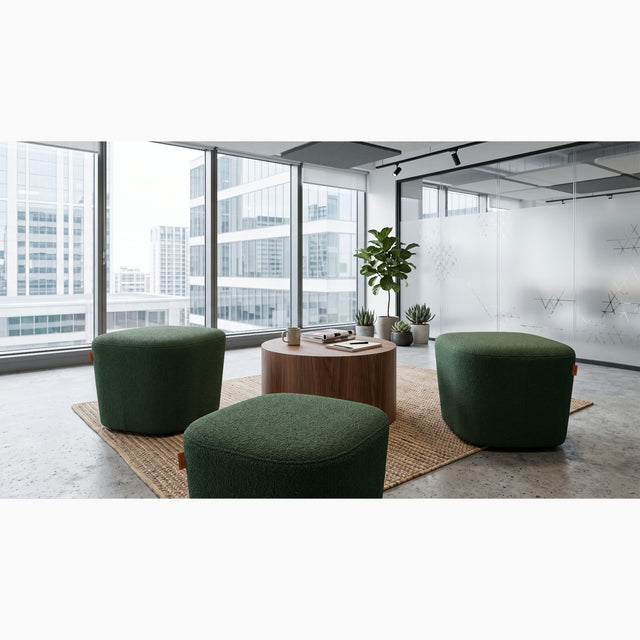 Three green Petal poufs arranged around a round wooden coffee table in a communal area of a modern office, with lots of natural light and city views.