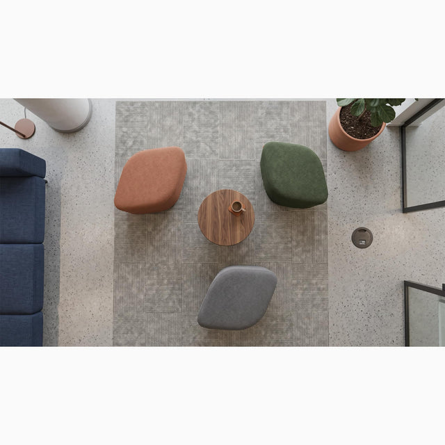 Overhead view of three Petal poufs in terracotta, sage green and grey fabrics, arranged around a small round wooden coffee table in a break area in a modern office.