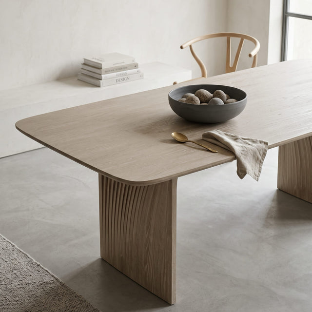 A close up view of the Sheer dining table in white Oak. The table is in a bright, minimalist dining room with stone washed walls and a concrete floor.
