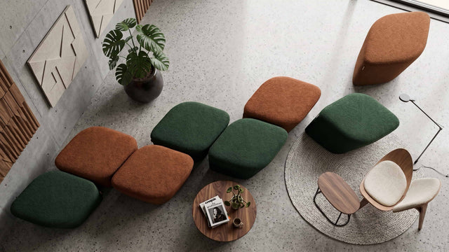 A modern lounge area in a public space with multiple upholstered ottomans in green and rust orange, neatly arranged in a line to keep things tidy and uncluttered when not in use.