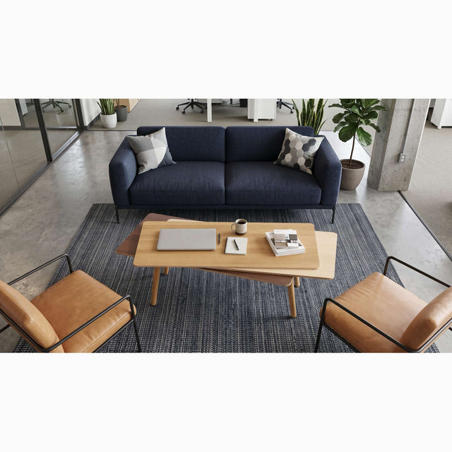 A wooden Stacked Coffee table centred between a blue sofa and 2 leather armchairs in a communal seating area of a modern office.