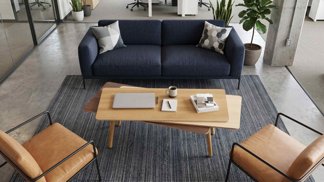 A wooden Stacked Coffee table centred between a blue sofa and 2 leather armchairs in a communal seating area of a modern office.