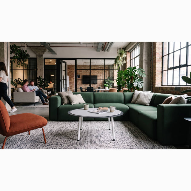 A white/light grey/dark grey Stacked coffee table provides a practical work surface for a modern green sectional sofa in a bright, industrial, loft-style work space.