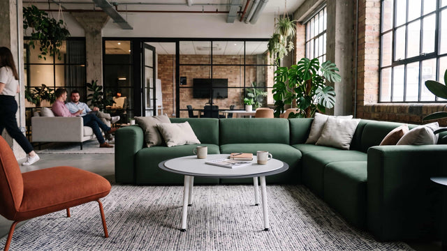 A white/light grey/dark grey Stacked coffee table provides a practical work surface for a modern green sectional sofa in a bright, industrial, loft-style work space.