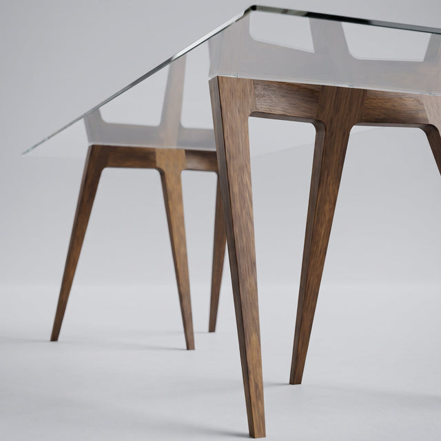 A close-up studio shot of the Flex trestle dining table legs in Walnut, showing its elegant form and beautiful joinery, with a clear glass table top.