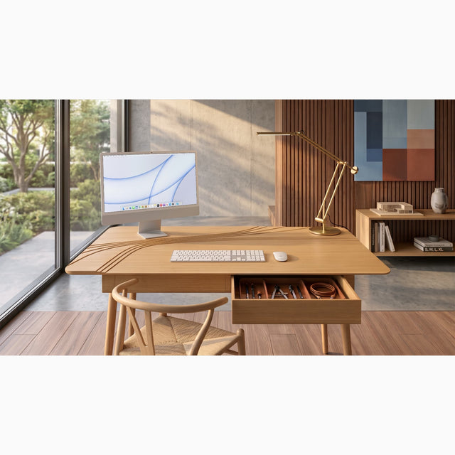 An Oak version of the Terrace Desk takes pride of place within a quiet corner of a contemporary home office. A monitor is positioned on the elevated left corner of the desk to offer a better eye line, and a lamp in placed on the dedicated space on the right corner of the desk. A keyboard and mouse are positioned on the desk's large, main work surface.