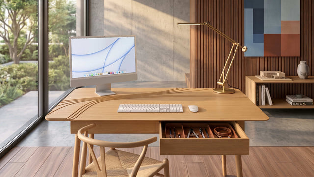An Oak version of the Terrace Desk takes pride of place within a quiet corner of a contemporary home office. A monitor is positioned on the elevated left corner of the desk to offer a better eye line, and a lamp in placed on the dedicated space on the right corner of the desk. A keyboard and mouse are positioned on the desk's large, main work surface.