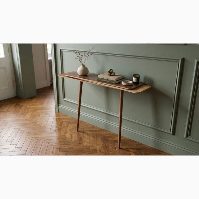A sage green wall panelled hallway features a wooden Stacked console table on a herringbone wood floor. The console is made up of a Walnut top surface, Ash middle and Oak bottom, with two Walnut legs.