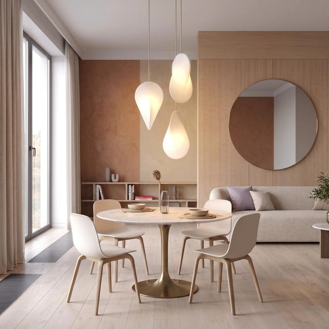 Three Oh Lloyd! pendant lights hang at staggered heights over a round table in a modern dining space. The lights are turned on, giving a soft illumination, and their orientations vary, displaying three different profiles of Oh Lloyd's unique form.
