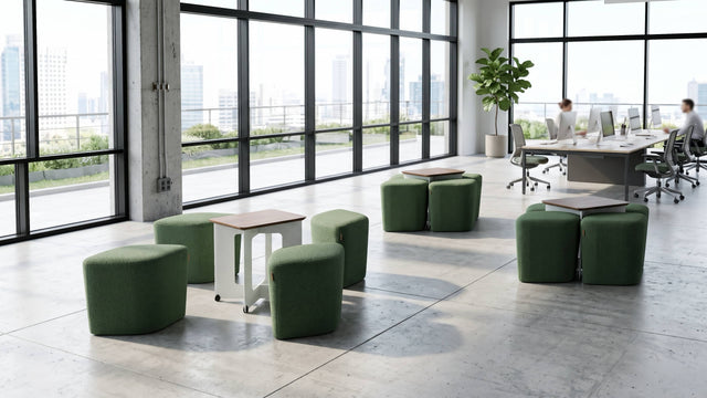 A communal space in an open plan office features three Rhombic seating systems with green poufs and walnut tables. One Rhombic system has its poufs pulled out from under its table ready for use, while the other two systems remain neatly squared away.