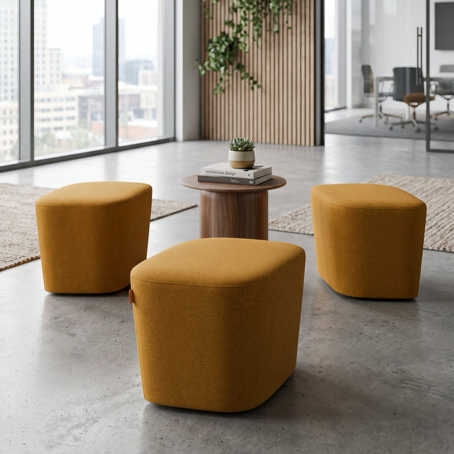 Three mustard yellow fabric Petal poufs arranged around a small round wooden side table in a breakout area of a modern office.