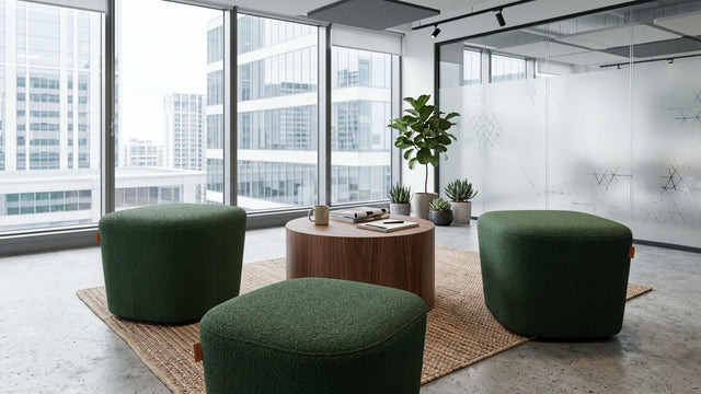 Three green Petal poufs arranged around a round wooden coffee table in a communal area of a modern office, with lots of natural light and city views.
