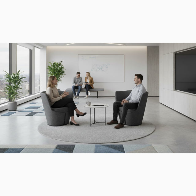 Two people having a conversation whilst sat on grey Dapper armchairs in a communal office space.