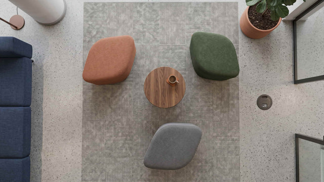 Overhead view of three Petal poufs in terracotta, sage green and grey fabrics, arranged around a small round wooden coffee table in a break area in a modern office.