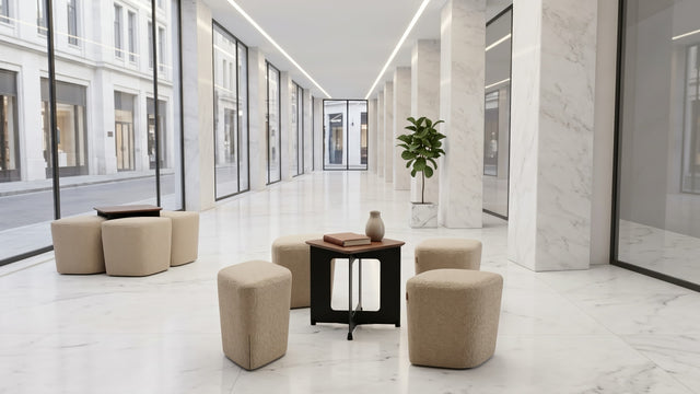 A marble lined lobby houses two Rhombic seating systems with tables. The poufs are upholstered in a pale brown fabric, and the tables have black frames with walnut tabletops.